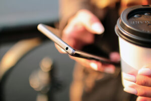 Person med mobiltelefon i den ene hånd og takeaway-kaffe i den anden.